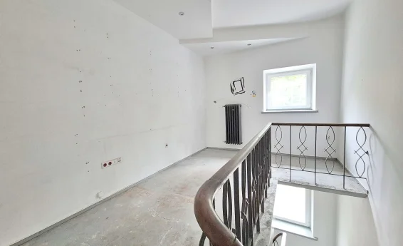 Antresola lokalu usługowego z metalową balustradą, oknem oraz schodami prowadzącymi na niższą kondygnację.