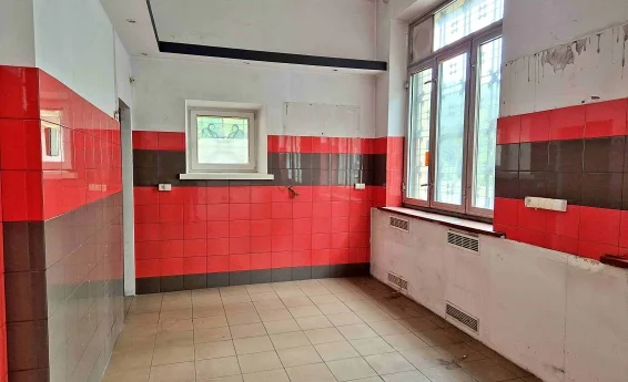 Pomieszczenie lokalu usługowego z czerwono-grafitową okładziną ścienną, dużymi oknami oraz przygotowaną instalacją pod zabudowę.